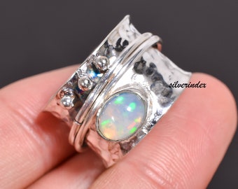 May include: A silver spinning ring with a white opal gemstone. The ring has a hammered texture and a band that spins freely.