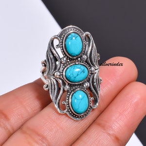 May include: A silver ring with an intricate design featuring three turquoise stones. The ring has a delicate, ornate look and is a statement piece.