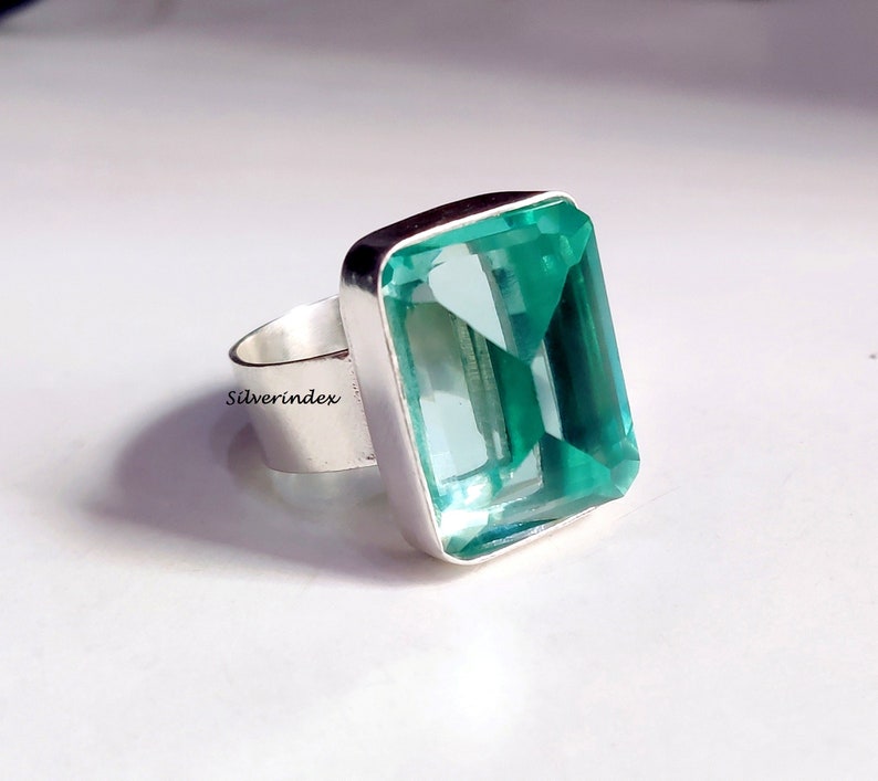May include: A silver ring with a large, rectangular, light blue gemstone. The gemstone is faceted and has a clear, glassy appearance.