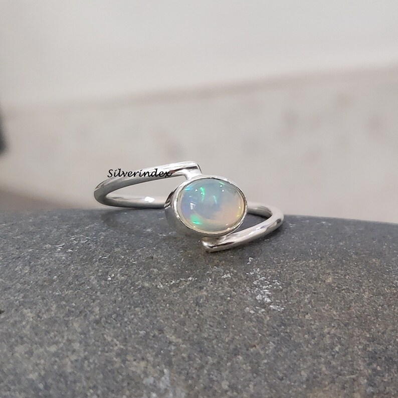 May include: A silver ring with a white opal gemstone. The ring has a simple, modern design with a curved band.