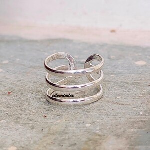 May include: A silver-colored ring with a unique design. The ring features three horizontal bands connected by a vertical loop. The word "silverindex" is engraved on the ring. The ring is made of a shiny, metallic material.