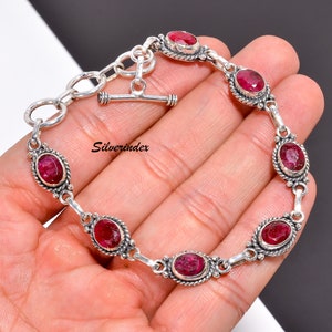 Può includere: Un braccialetto d'argento con chiusura a scorrimento presenta sei pietre preziose rosse di forma ovale. Il braccialetto è in argento sterling e ha un design delicato.