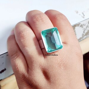 May include: A silver ring with a large, light green, emerald-cut gemstone. The ring is on a person's finger.