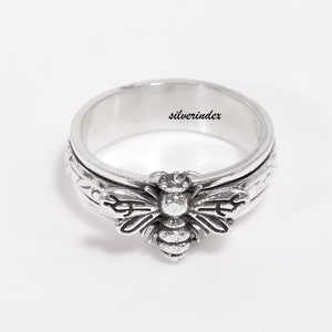 May include: A silver spinning ring with a bee design. The ring has a textured band and the bee is detailed with wings and a stinger.