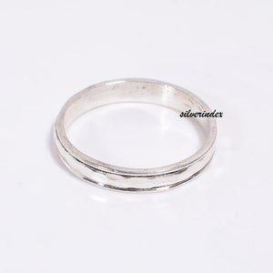 May include: A silver band ring with a textured design. The ring is simple and elegant.