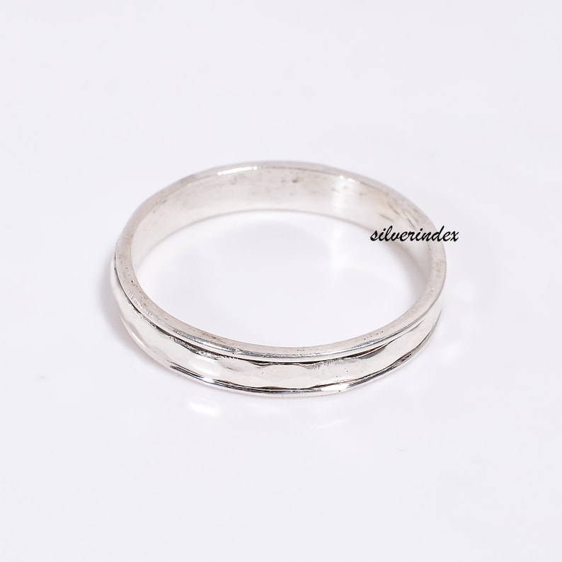 May include: A silver band ring with a textured design. The ring is simple and elegant.