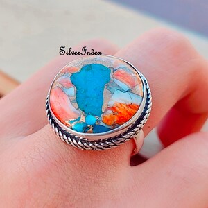 May include: A silver ring with a large, round turquoise and coral stone. The stone is a mix of blue, orange, and white.