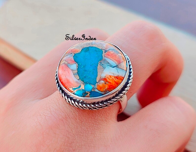 May include: A silver ring with a large, round turquoise and coral stone. The stone is a mix of blue, orange, and white.