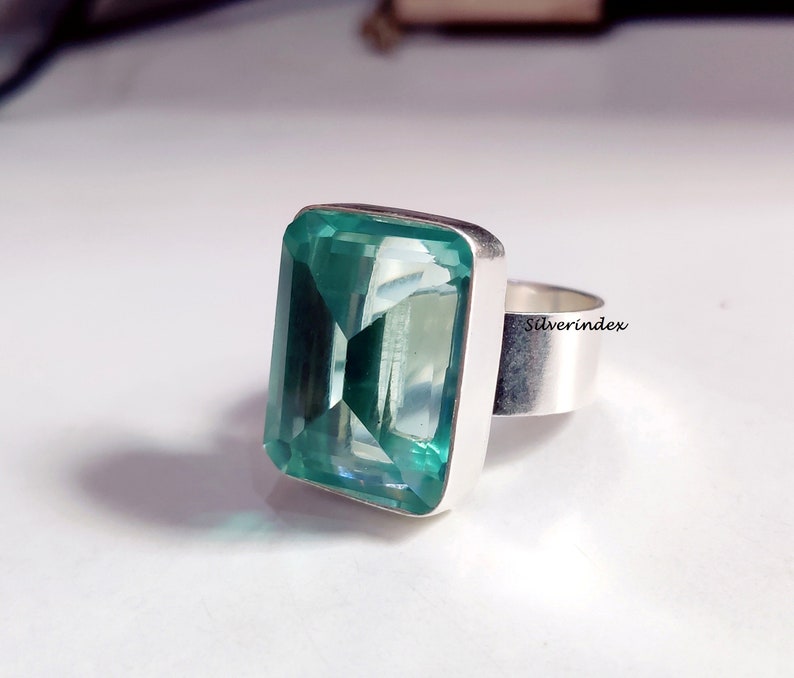 May include: A silver ring with a large, emerald green gemstone. The gemstone is cut into a rectangular shape with beveled edges. The ring is set in a simple, silver band.