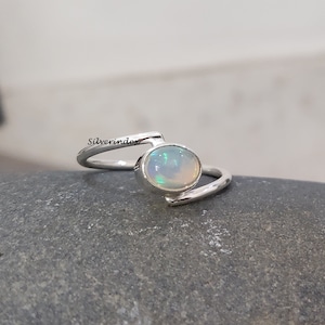 May include: A silver ring with a white opal gemstone. The ring has a simple, modern design with a curved band.