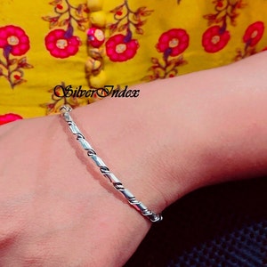 May include: A silver bangle bracelet with a twisted design. The bracelet is on a person's wrist.