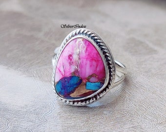 May include: A silver ring with a pink, blue, and brown gemstone set in a rope-like border.