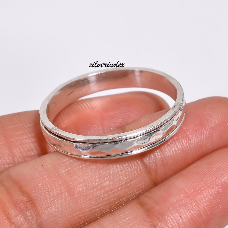 May include: A silver spinning ring with a hammered texture. The ring is worn on a finger.