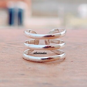 May include: A silver-colored ring with a three-tiered design. The ring has a smooth, polished finish and a modern, minimalist aesthetic. The word "silverindex" is engraved on the ring. This ring is a piece of jewelry.