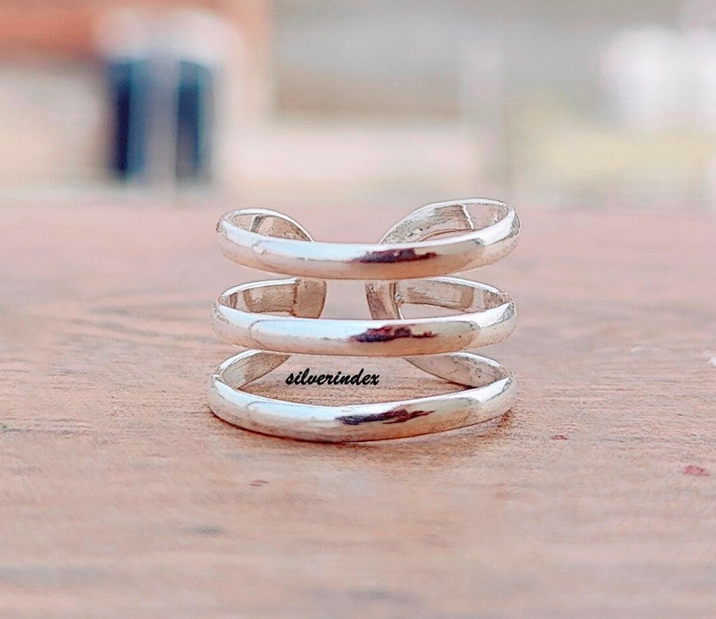 May include: A silver-colored ring with a three-tiered design. The ring has a smooth, polished finish and a modern, minimalist aesthetic. The word "silverindex" is engraved on the ring. This ring is a piece of jewelry.