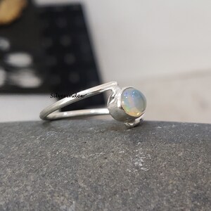 May include: A silver ring with a white opal gemstone. The ring is set on a gray stone background.