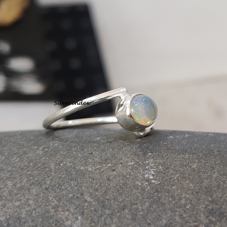 May include: A silver ring with a white opal gemstone. The ring is set on a gray stone background.