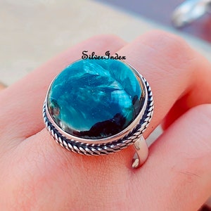 May include: A silver ring with a large, round, green gemstone. The gemstone has a swirling pattern and a dark green center. The ring has a rope-like band.