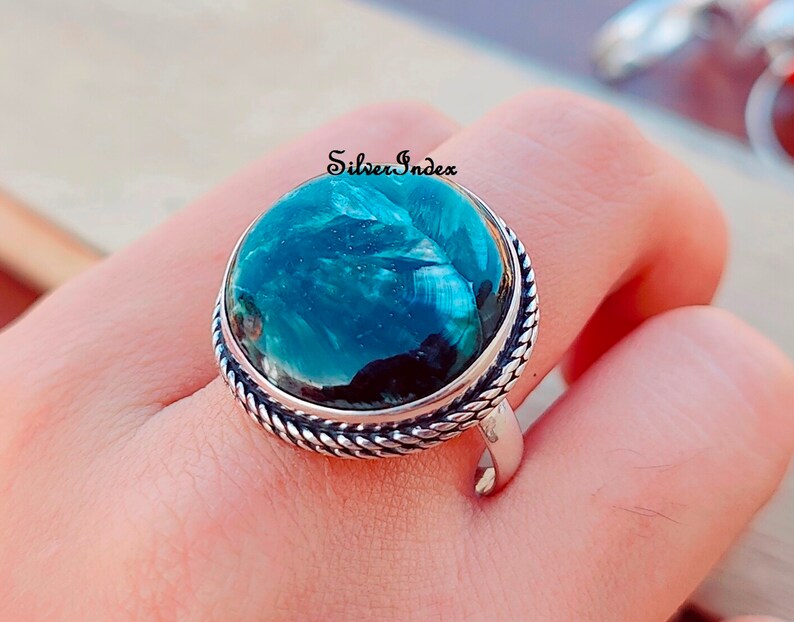 May include: A silver ring with a large, round, green gemstone. The gemstone has a swirling pattern and a dark green center. The ring has a rope-like band.