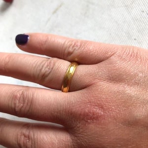 May include: A simple gold band ring with a slightly textured surface.