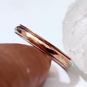 May include: A hammered rose gold band ring. The ring is simple and elegant, with a smooth, polished finish.