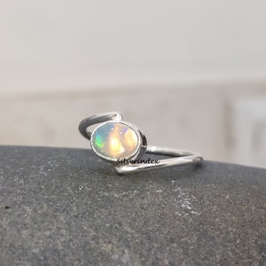 May include: A silver ring with a white opal gemstone. The ring has a simple, elegant design with a curved band.