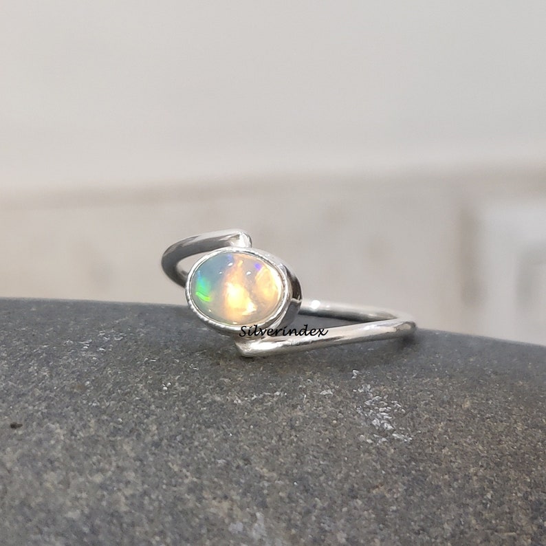 May include: A silver ring with a white opal gemstone. The ring has a simple, elegant design with a curved band.
