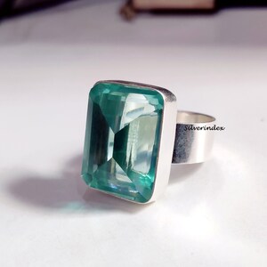 May include: A silver ring with a large, emerald green gemstone. The gemstone is cut into a rectangular shape with beveled edges. The ring is set in a simple, silver band.