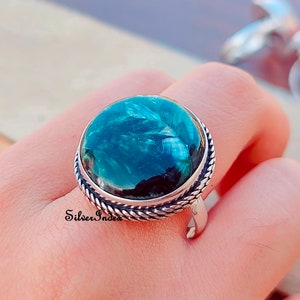 May include: A silver ring with a large, round, green gemstone set in a rope-like band. The gemstone has a swirling, marbled pattern.