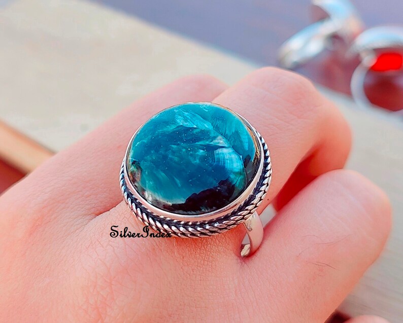 May include: A silver ring with a large, round, green gemstone set in a rope-like band. The gemstone has a swirling, marbled pattern.