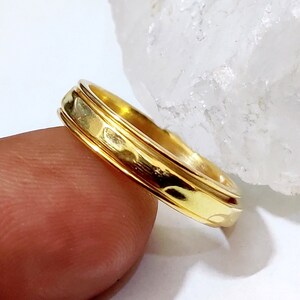May include: A gold band ring with a textured design. The ring is worn on a finger.