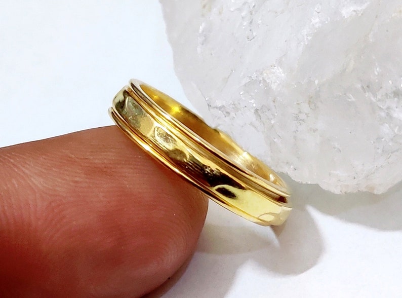 May include: A gold band ring with a textured design. The ring is worn on a finger.
