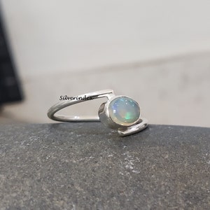 May include: A silver ring with a white opal gemstone. The ring has a simple, modern design with a curved band.