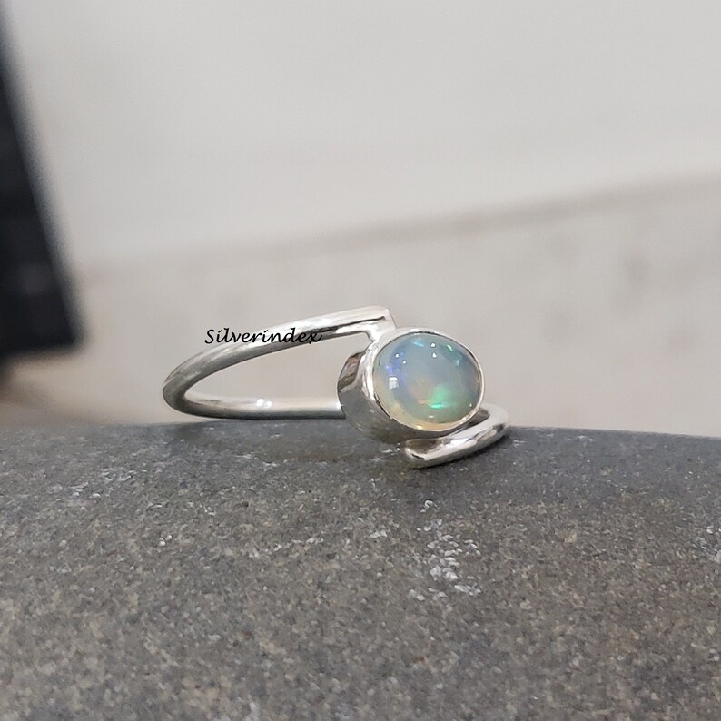 May include: A silver ring with a white opal gemstone. The ring has a simple, modern design with a curved band.