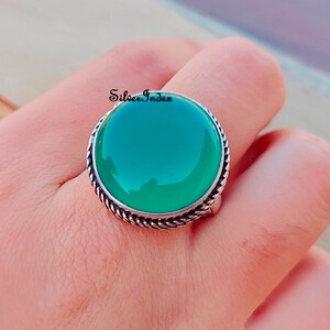 May include: A silver ring with a large, round, green gemstone set in a twisted silver band. The ring is on a finger.