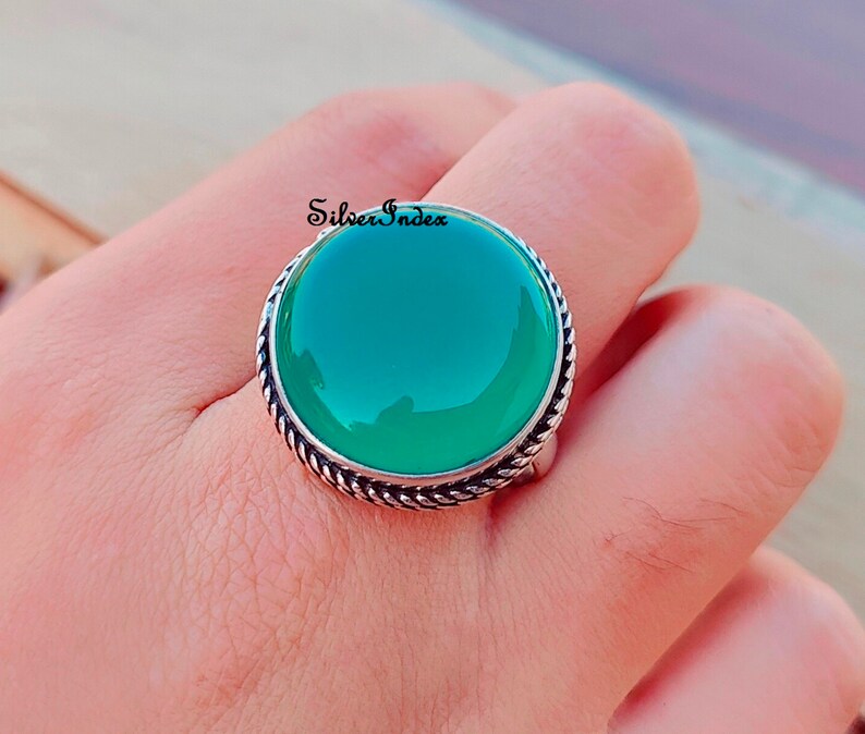 May include: A silver ring with a large, round, green gemstone set in a twisted silver band. The ring is on a finger.