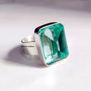May include: A silver ring with a large, rectangular, light blue gemstone. The gemstone is faceted and has a clear, glassy appearance.