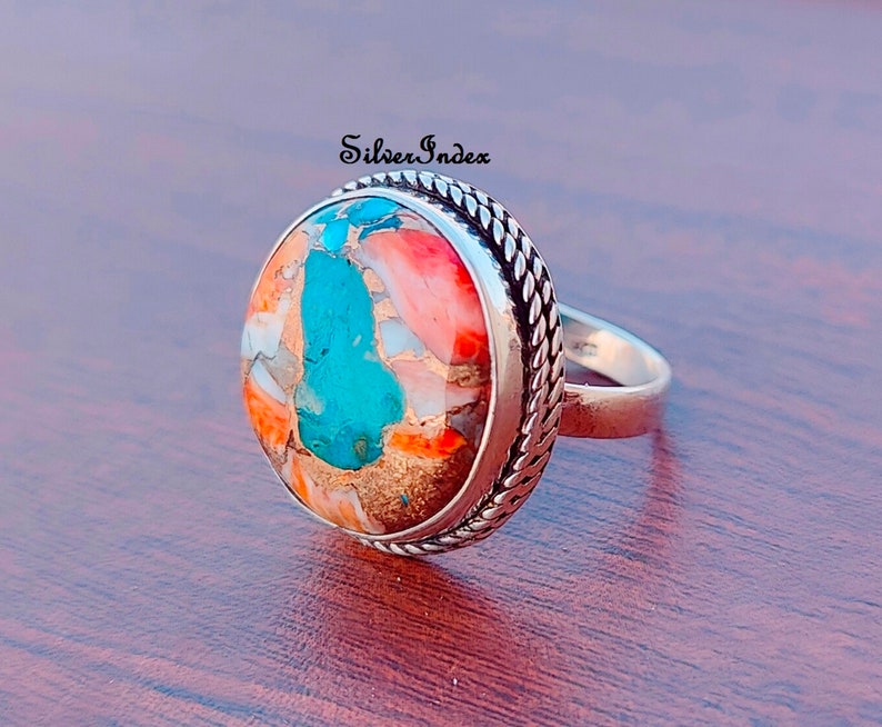 May include: A silver ring with a large, oval-shaped turquoise and coral stone set in a rope-like border.