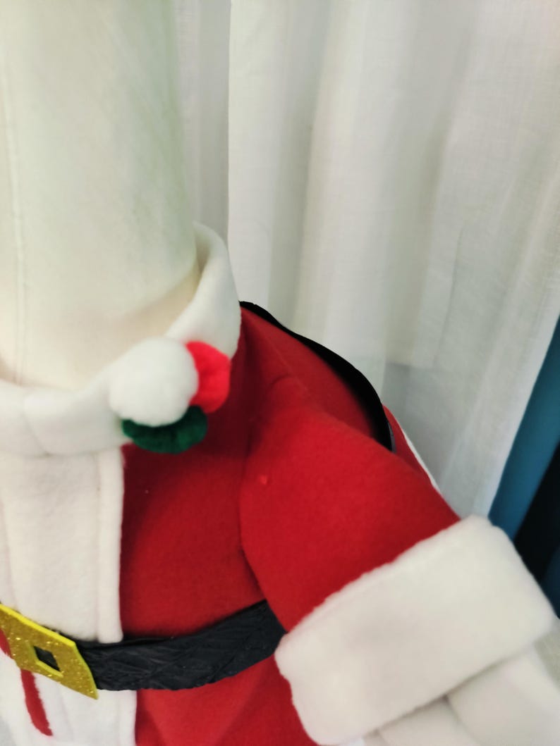 May include: A Santa Claus costume with a red jacket, white faux fur trim, and a black belt with a gold buckle. The costume includes a white collar and a matching hat with a red and green pom-pom. The outfit is designed for festive holiday celebrations.