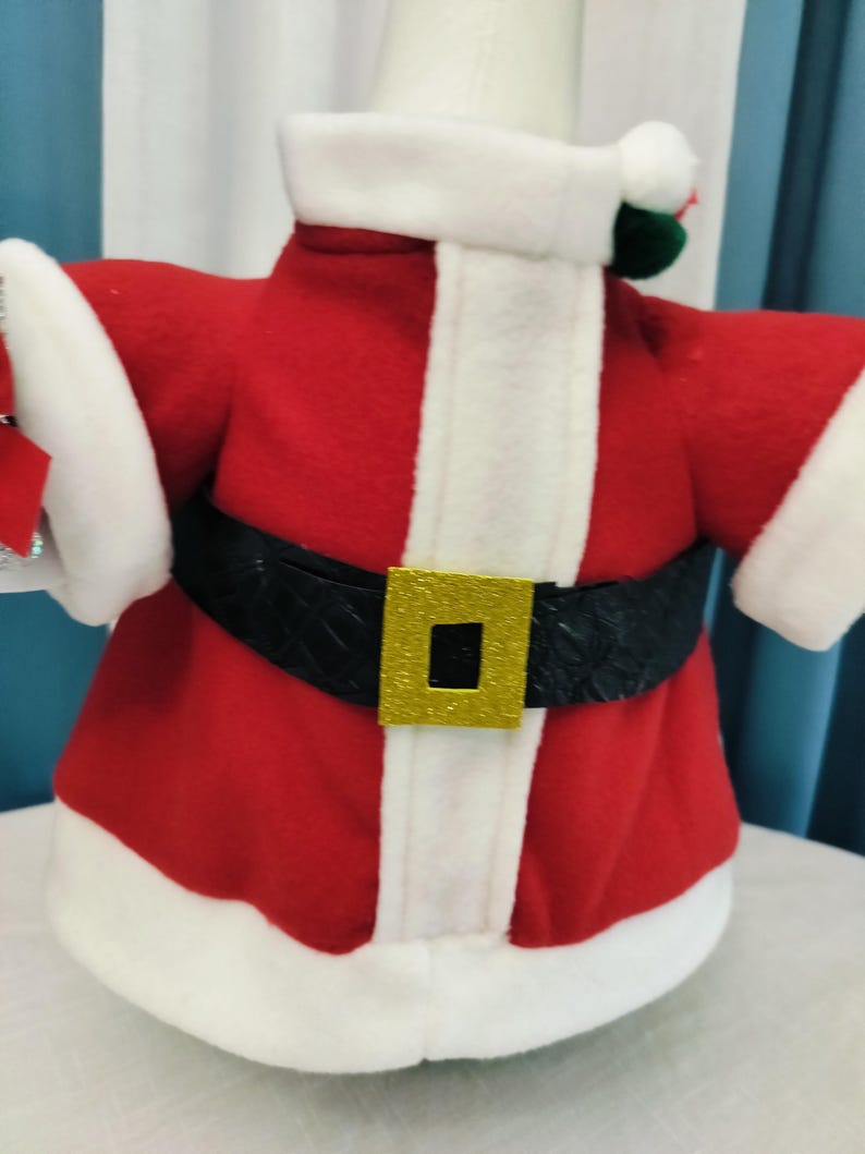 May include: A festive Santa Claus costume for a decorative item. The outfit features a red jacket with white trim, a black belt with a gold buckle, and white cuffs. The costume is designed to fit around a cylindrical object.