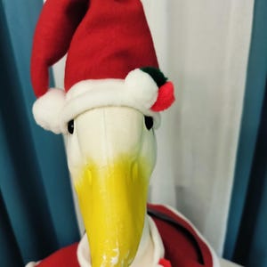 May include: A plush duck dressed in a Santa Claus outfit. The duck has a white head and a yellow beak. It wears a red Santa hat with white trim and a red coat with white trim. The duck is a festive holiday decoration.
