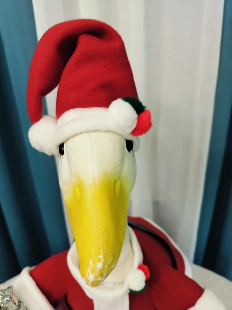 May include: A plush duck dressed in a Santa Claus outfit. The duck has a white head and a yellow beak. It wears a red Santa hat with white trim and a red coat with white trim. The duck is a festive holiday decoration.