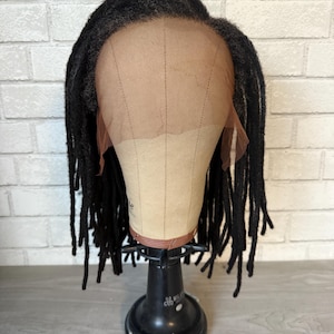 May include: Black dreadlock wig on a wig stand. The wig is made of synthetic hair and has a lace front.