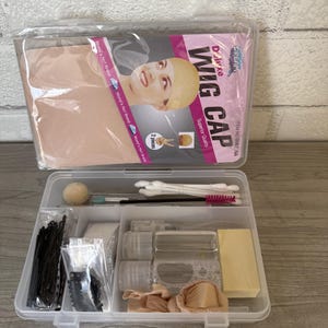 以下が含まれることがあります： ウィッグアクセサリーが入った透明なプラスチックケース。ケースには「WIG CAP」と「Superior Quality」の文字が入ったウィッグキャップのパッケージが含まれています。中にはヘアピン、アプリケーター、小さなボトル、スポンジが入っています。