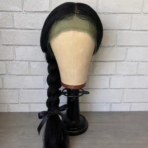 May include: A black braided lace front wig styled into a single long side braid. The wig features fine micro-braids throughout, a sheer lace front panel, and a black ribbon tied at the base of the braid. It is displayed on a mannequin head.