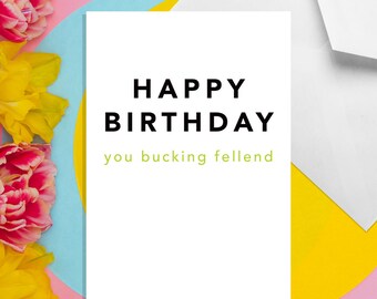 May include: A white card with the text "HAPPY BIRTHDAY you bucking fellend" in black and green lettering. The card is on a pink, blue, and yellow background.