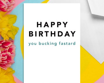 May include: A white card with the text "HAPPY BIRTHDAY you bucking fastard" in black and teal lettering on a pink, blue, and yellow background.