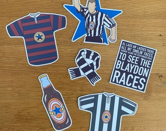 Puede incluir: Un conjunto de cinco pegatinas que representan una camiseta de fútbol a rayas blancas y negras, una bufanda a rayas blancas y negras, una estrella azul con un árbitro con una camiseta a rayas blancas y negras, una botella marrón con una estrella blanca y una camiseta de fútbol a rayas blancas y negras con el texto "AL LADS AN LASSES THERE. ALL WI SMILIN' FACES. GANNIN' ALONG THE SCOTSWOOD ROAD TO SEE THE BLAYDON RACES".