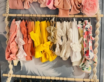 May include: A wooden rack with three tiers holds a variety of colorful headbands with bows. The headbands are arranged in rows and are made of different fabrics, including velvet, satin, and cotton. The headbands are in shades of pink, yellow, blue, green, and black.