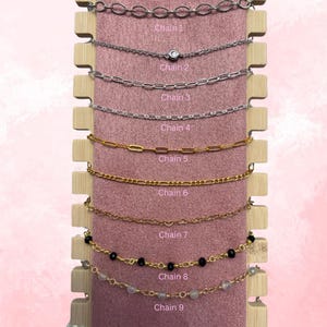 May include: Nine different chain styles displayed on a pink background. The chains are arranged vertically, with the top chain being the most delicate and the bottom chain being the most substantial. The chains are labelled with numbers 1 through 9.
